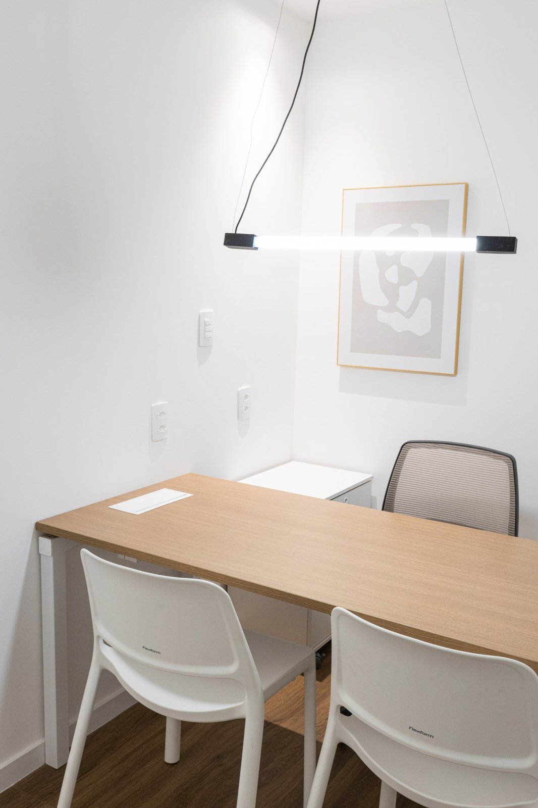 Consultório com mesa de madeira, cadeiras e luminária pendente