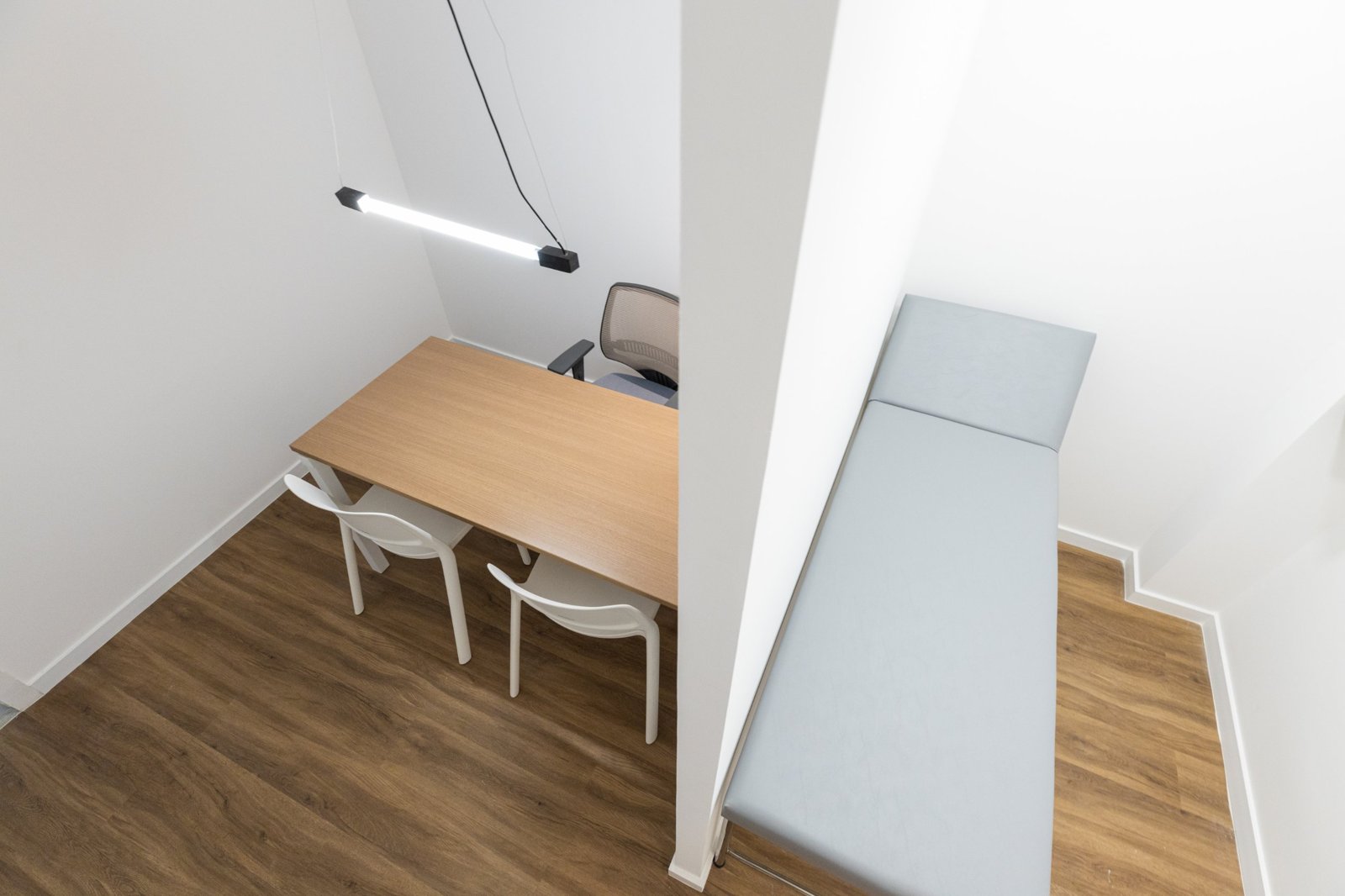 Consultório visto de cima, com mesa de um lado e maca do outro